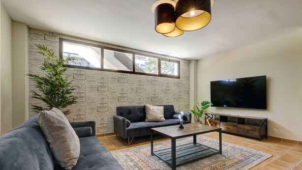 Una sala de estar moderna con un sofá gris, una mesa de centro, un televisor y una pared con decoración en caligrafía.