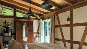 A bedroom with a large bed, wooden beams, a bookshelf, and a window with curtains. - Holiday Home Farmhouse in Altes Forsthaus Boppard (Boppard)