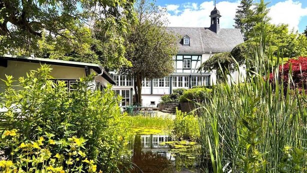 A traditional building with a garden pond, surrounded by lush greenery and flowering plants. - Holiday Home Farmhouse in Altes Forsthaus Boppard (Boppard)