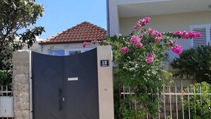 Une entrée fermée par un portail surmonté d’un panneau indiquant un numéro, un mur de pierre et un bâtiment doté d’un toit en tuiles.