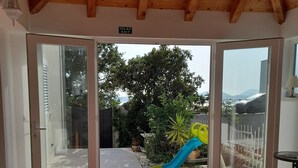 Une pièce spacieuse avec un plafond haut et un sol carrelé, qui donne sur un espace extérieur doté d’un toboggan et de verdure.