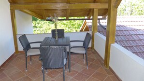 Un patio techado con una mesa y cuatro sillas, un jarrón con flores y vistas a la vegetación.