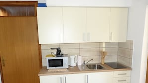 Una cocina compacta con armarios blancos, microondas, hervidor y lavabo.