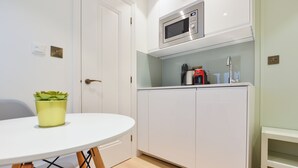 Eine kleine Küche mit weißen Schränken, einer Mikrowelle, einer Kaffeemaschine und einem kleinen Topfpflanzen auf einem weißen Tisch.