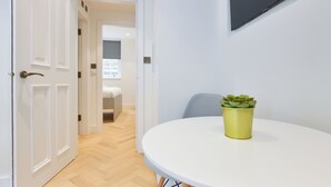 Ein modernes Zimmer mit einer weißen Tür, einem runden Tisch mit einer gelben Pflanze und einem Flachbildfernseher an der Wand.