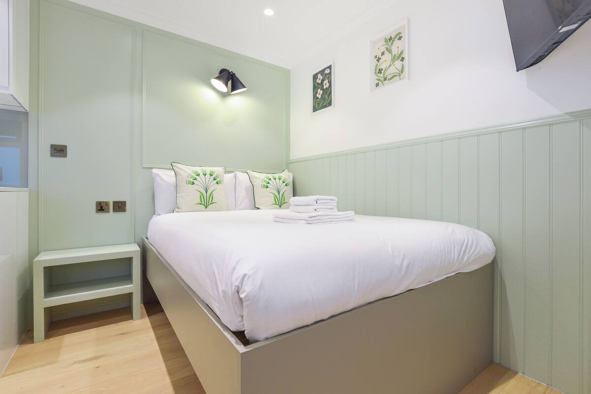 Un dormitorio con cama, mesitas de noche y una lámpara de pared.