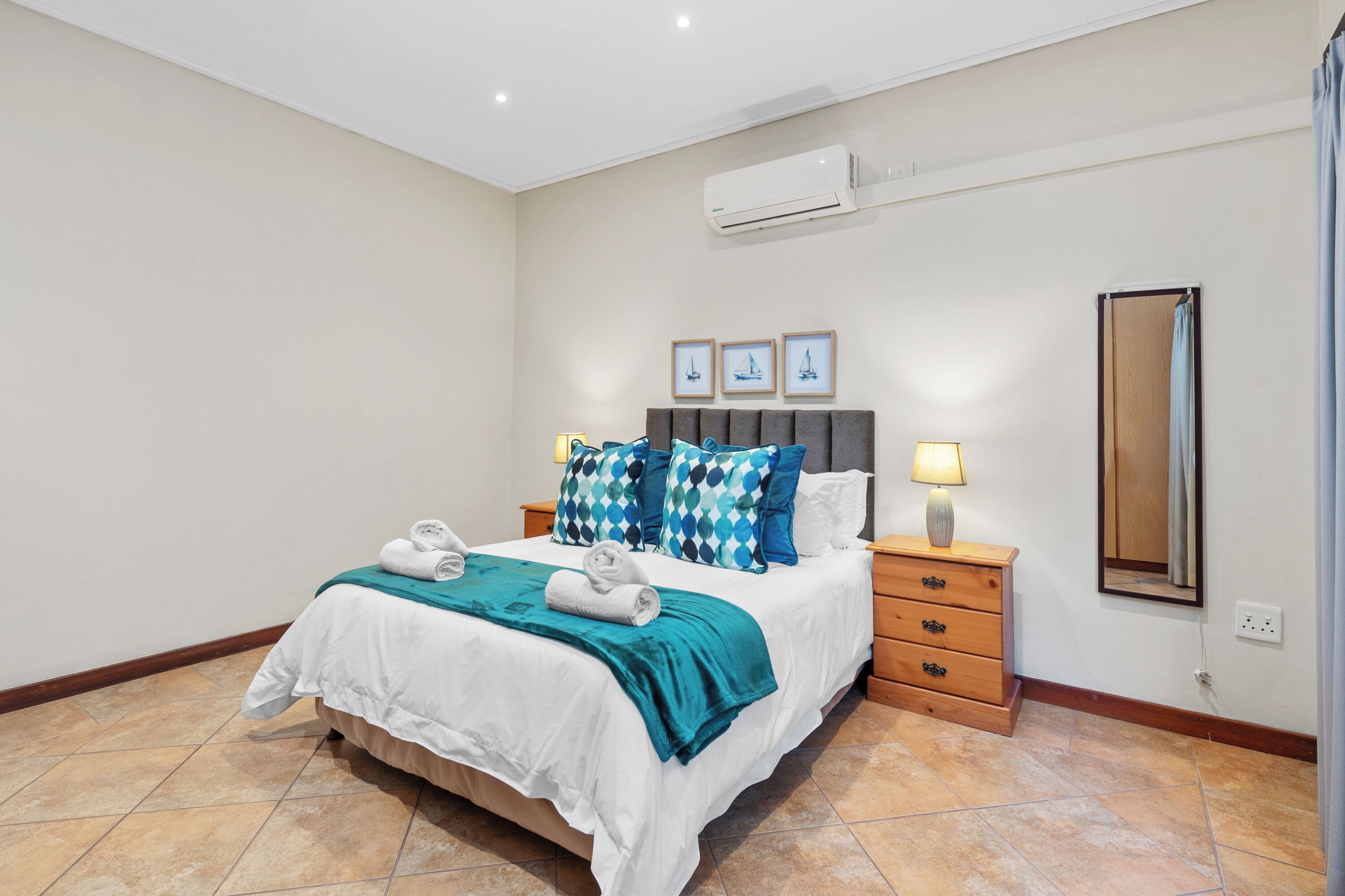 A neatly made bed with a teal throw blanket, a bedside lamp, and a wooden nightstand with drawers.