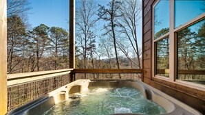 A hot tub with a digital control panel, surrounded by wooden deck and large windows offering a forest view.
