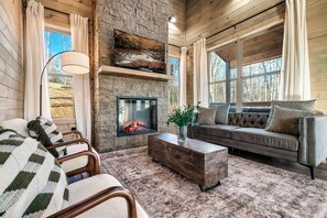 Ein gemütliches Blockhaus-Interieur mit Kamin aus Stein, einem großen, darüber montierten Fernseher, einer bequemen Couch und einem rustikalen Holztisch.