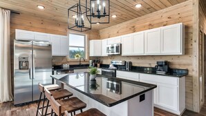 A modern kitchen with a central island, stainless steel appliances, white cabinetry, and wooden accents.