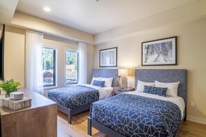 A modern hotel room with two beds, a desk, and a large window.