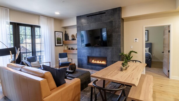 A modern living room with a fireplace, leather sofa, wooden dining table, and a TV mounted on the wall.