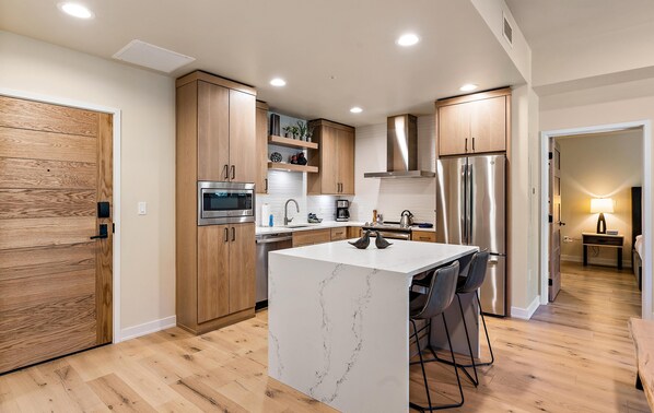 Una cocina moderna con armarios de madera, una isla de mármol y electrodomésticos de acero inoxidable.