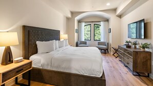 Une chambre d’hôtel moderne, dotée d’un grand lit, d’un bureau avec une lampe, d’une commode et d’un téléviseur fixé au mur.