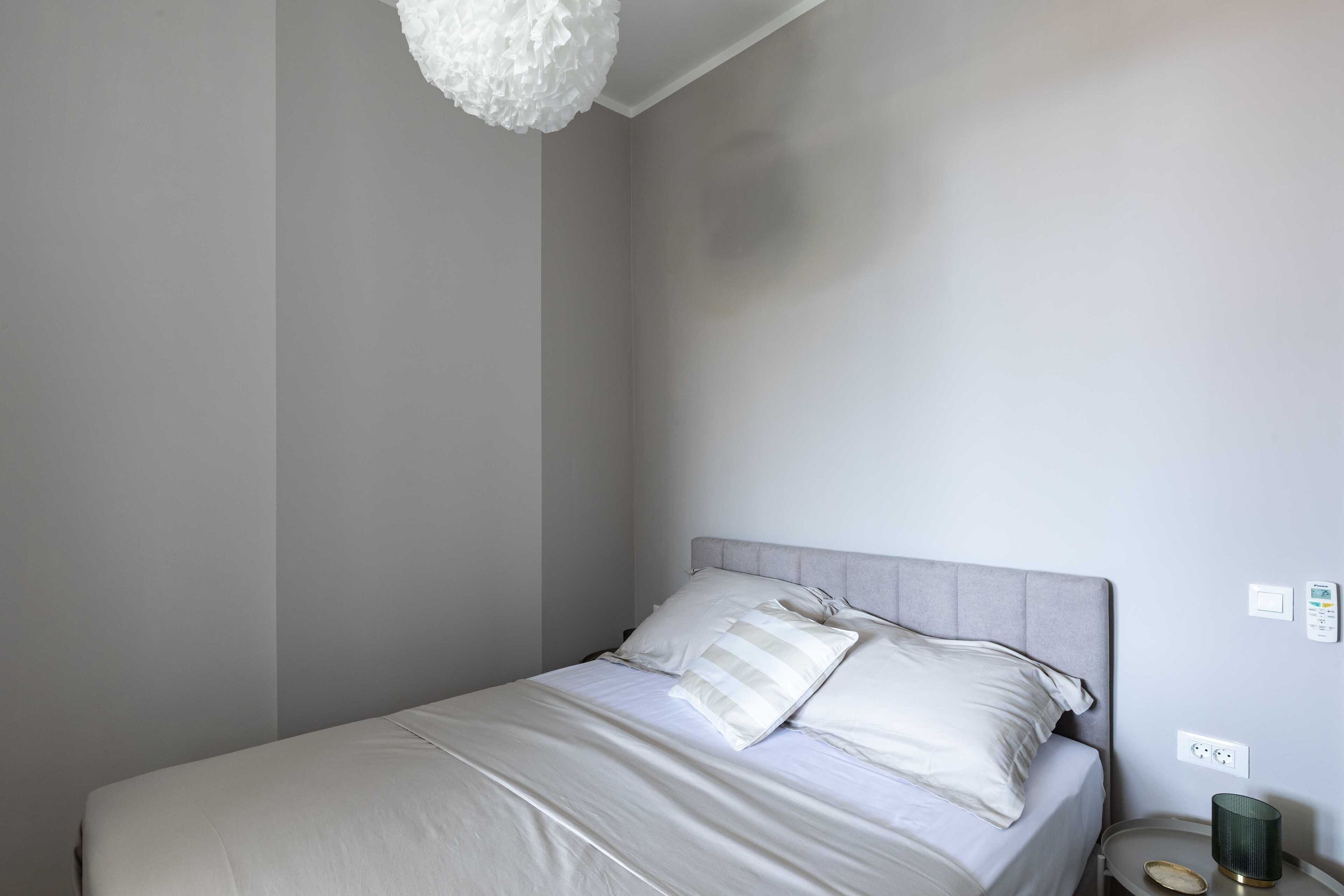 A neatly made bed with white linens and pillows, a grey headboard, and a bedside table with a green lamp.