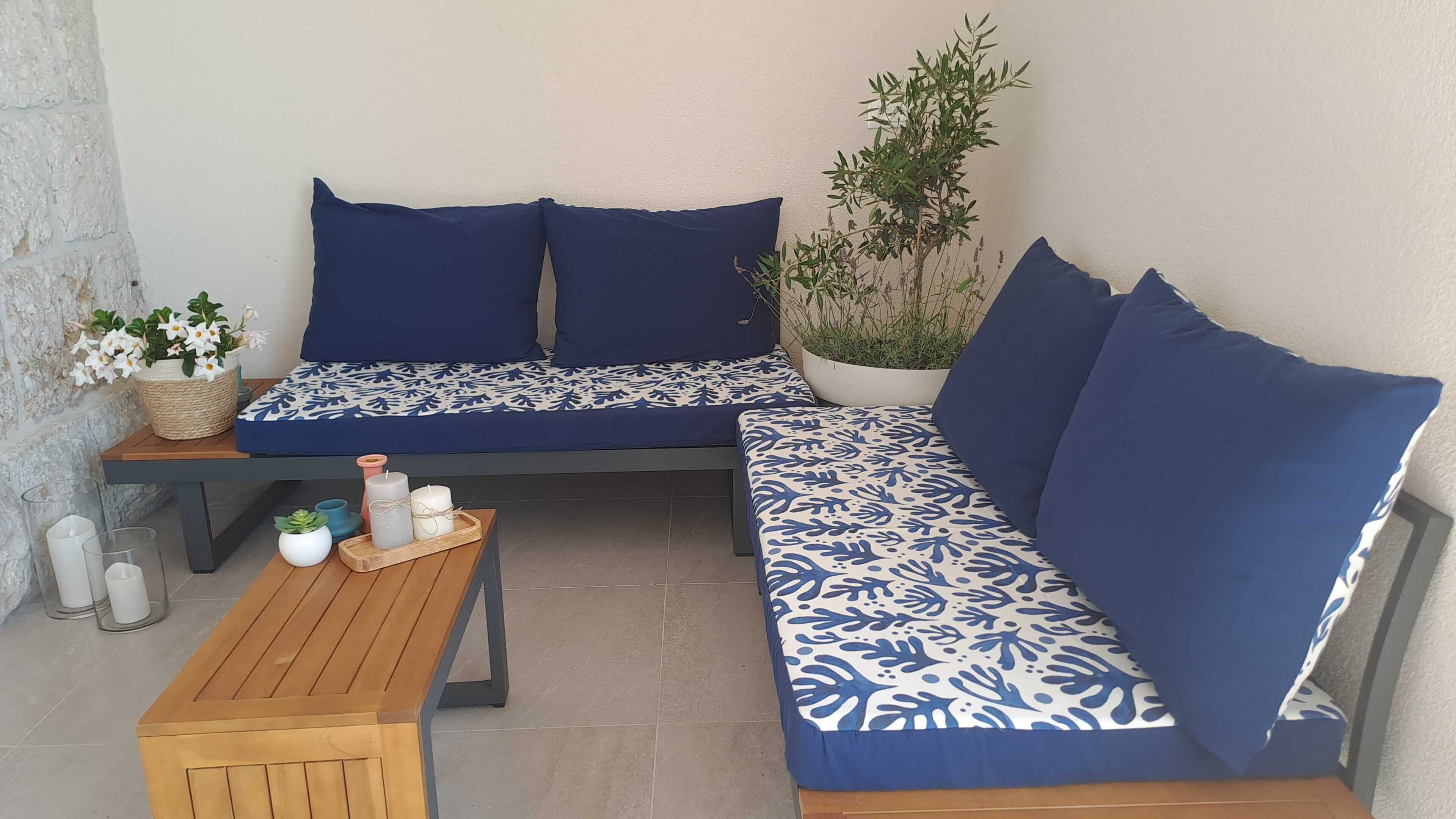 Ein gemütlicher Außenbereich mit einer Couch und einem Holztisch, mit einem Blumentopf und Kerzen.