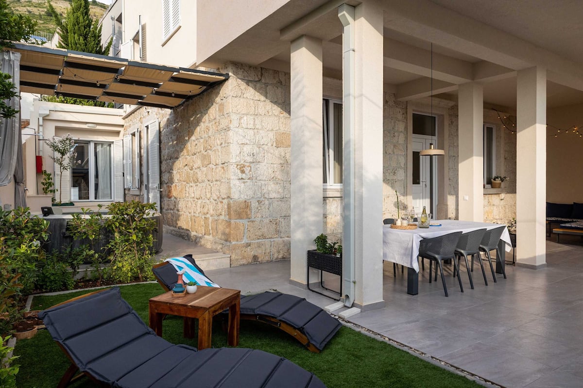 Eine überdachte Terrasse im Freien mit Esstisch, Stühlen und Liegestühlen.
