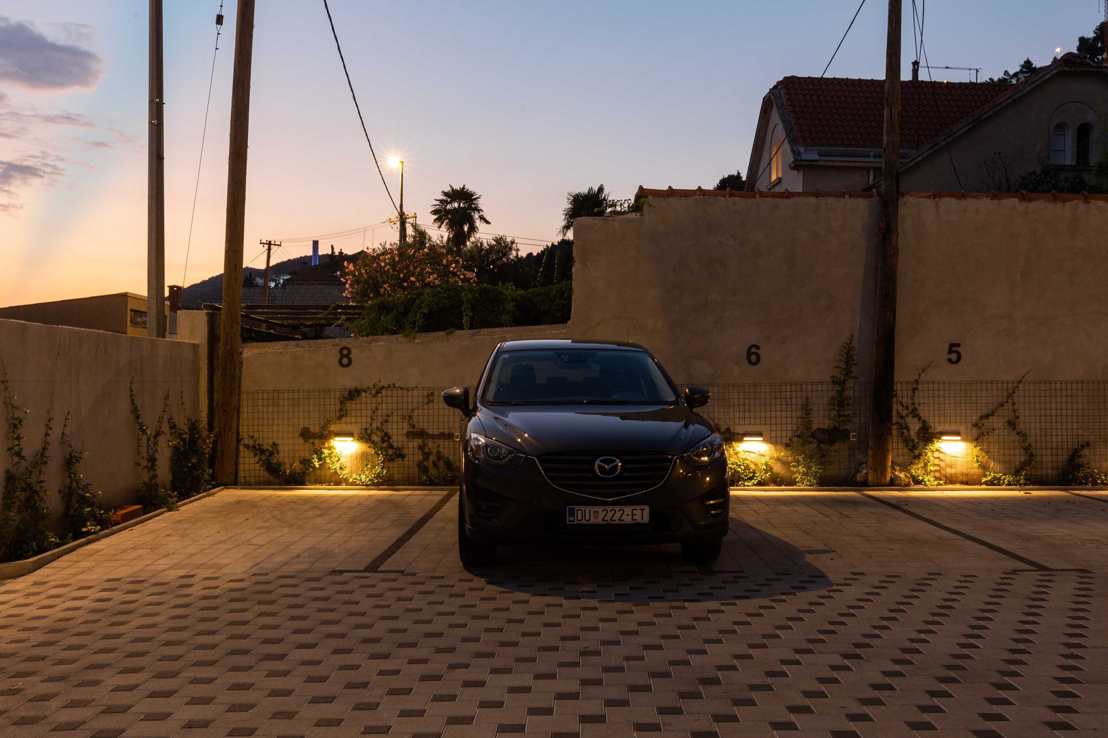 A car parked in a gated parking area with numbered gates and a paved walkway.