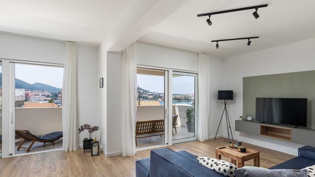 Ein modernes Wohnzimmer mit einer großen Couch, einem an der Wand befestigten Fernseher und einem Balkon mit Blick auf die Stadt.