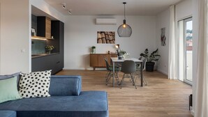 Ein modernes Wohnzimmer mit Sofa, Esstisch und Stühlen. Es gibt eine Küchenzeile mit Schränken und einer Pendelleuchte.