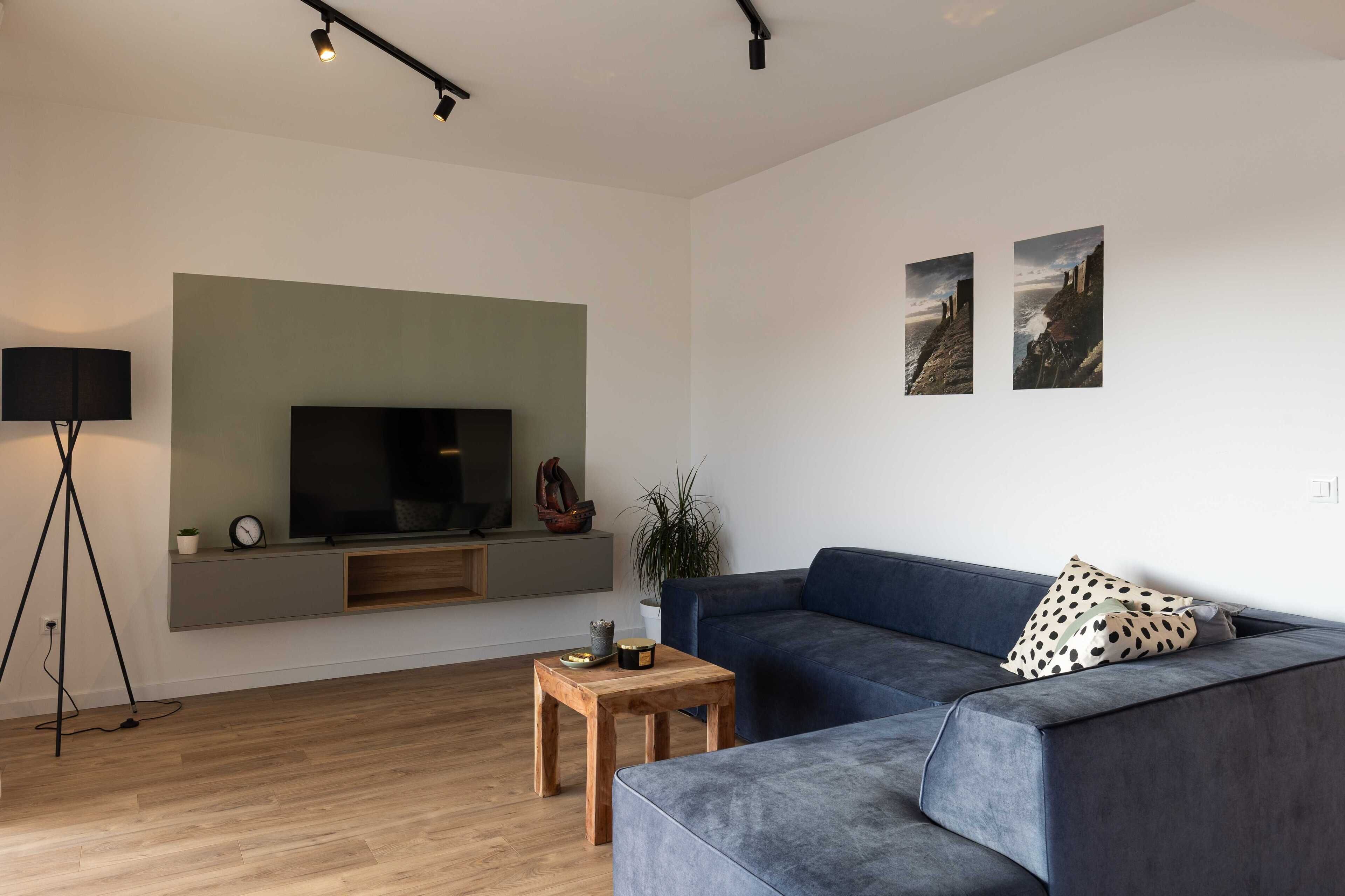 A modern living room with a grey sofa, a wooden coffee table, a mounted TV, and two wall-mounted pictures.