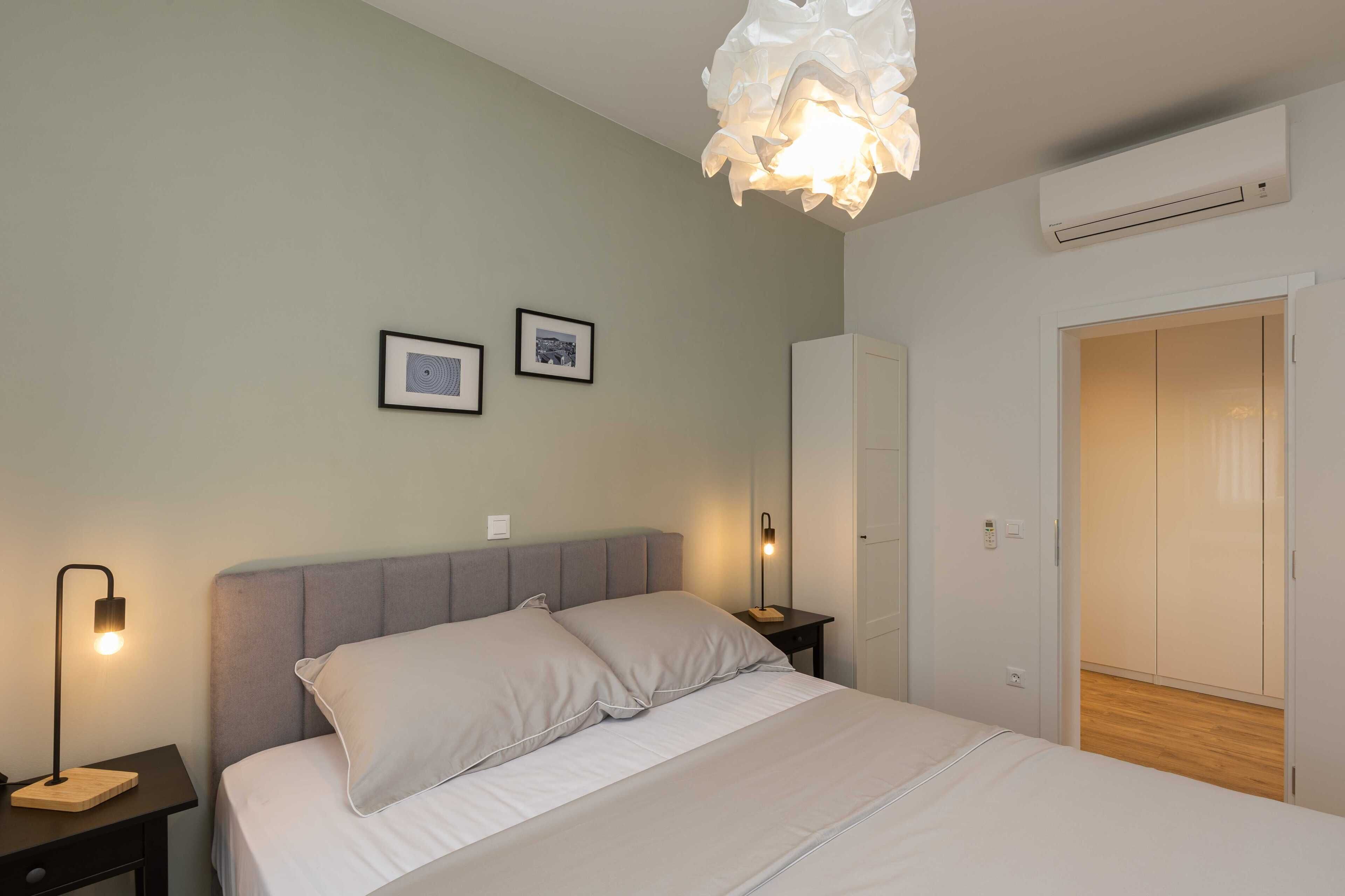 Un dormitorio con cama, lámparas de noche, armario y aire acondicionado de pared.