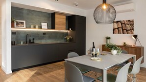 Eine moderne Küche mit Kochinsel, Pendelleuchten und einem Essbereich mit Tisch und Stühlen.