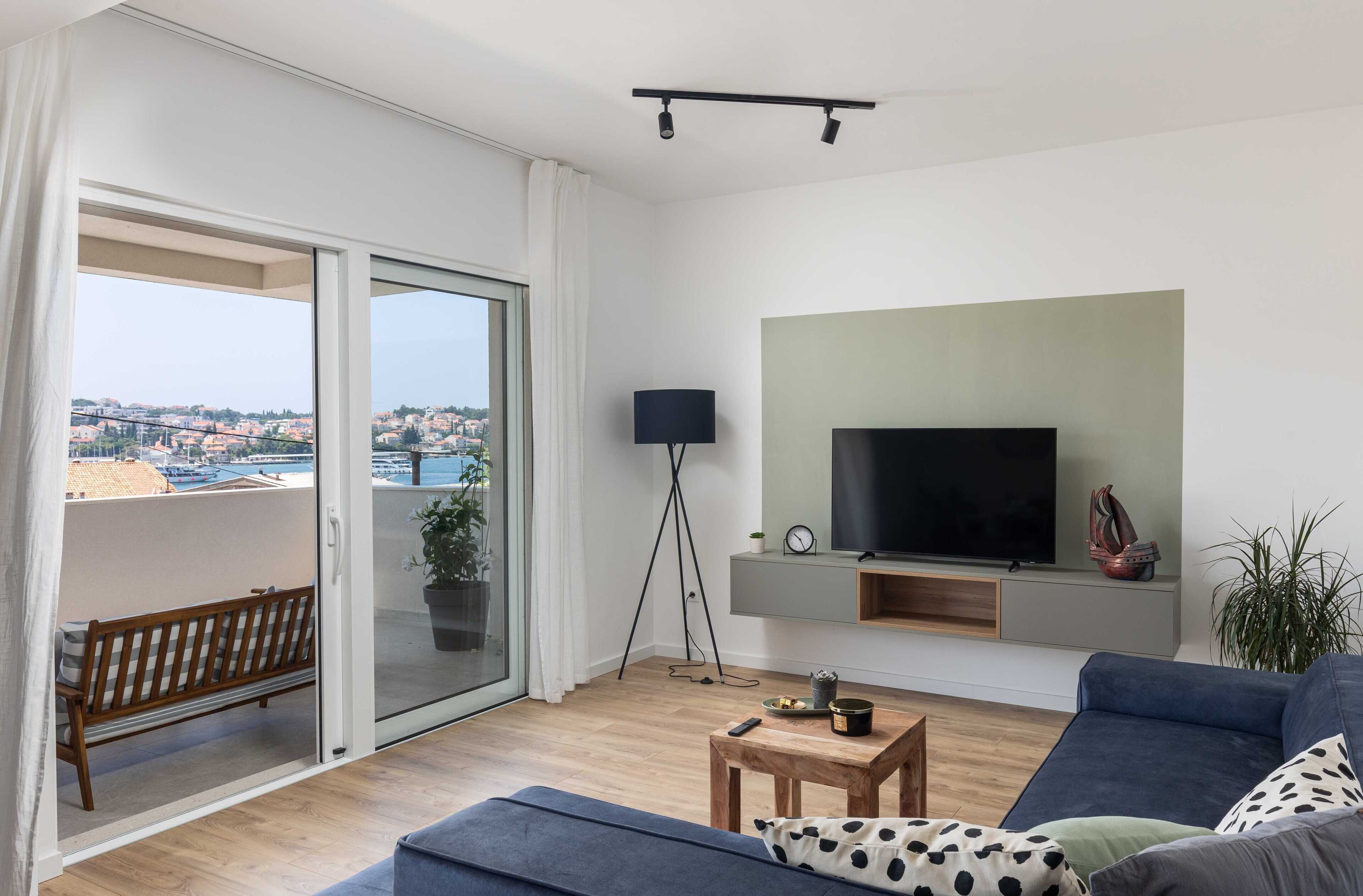 A modern living room with a large TV, a sofa, a coffee table, and a balcony with a bench.