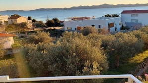 Zona residencial costera con casas, vista despejada al mar y un paisaje montañoso al fondo.