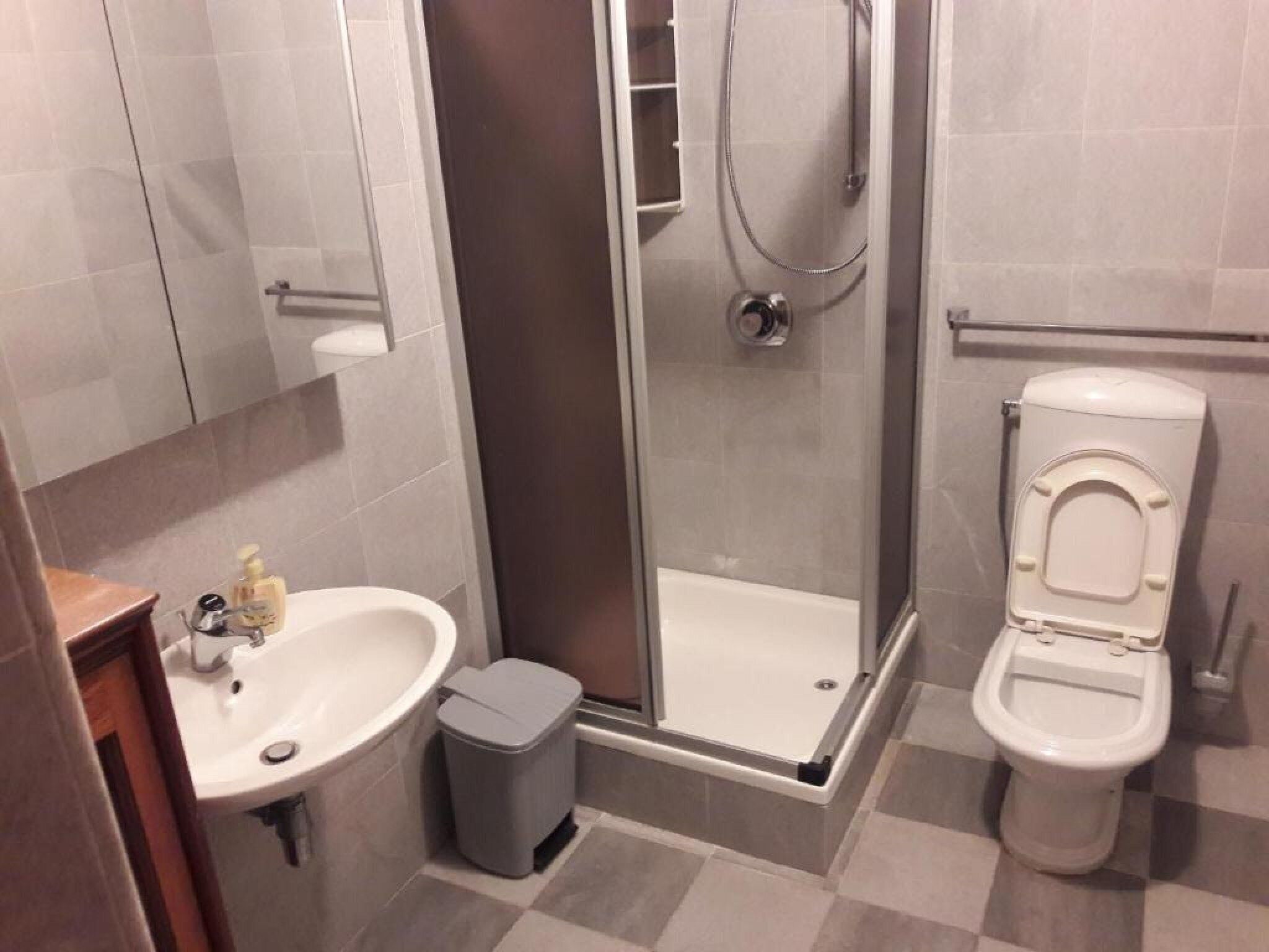 A bathroom with a shower, toilet, sink, and a trash bin.