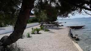 Un sendero de grava que conduce a un cuerpo de agua, bordeado por árboles y un muro blanco.