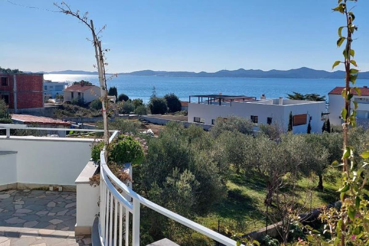 A residential area with a view of the sea, featuring a white building with a balcony and a garden.