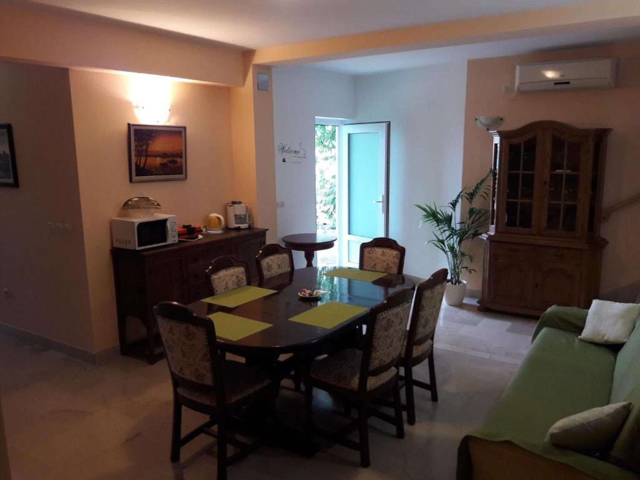 Ein Essbereich mit Tisch, Stühlen, einer Mikrowelle, einem Schrank und einem grünen Sofa.