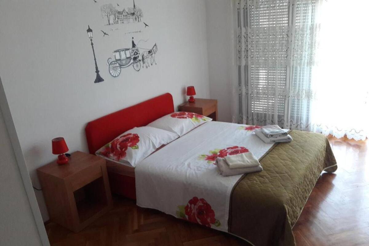 A bedroom with a bed, two bedside tables, a nightstand, and a window with curtains.