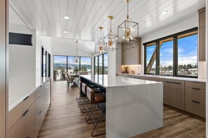 A modern kitchen with a large island, pendant lights, and a view of the outdoors.