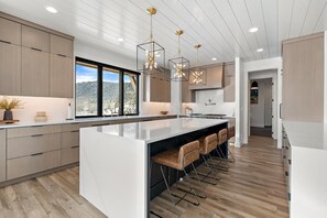 A modern kitchen with a large island, pendant lighting, and a view of the outdoors.