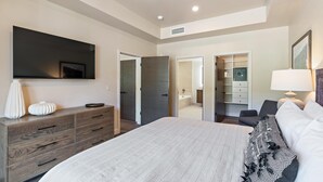 Un dormitorio moderno con una cama grande, un aparador, un televisor montado en la pared y un vestidor.