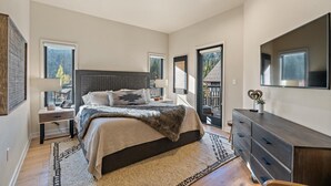 A bedroom with a large bed, a dresser, a TV, and a window with a view of trees. - Whispering Pines| Includes Two 1-Day Lift Tickets (Tamarack)