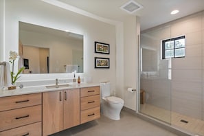 A modern bathroom with a large mirror, wooden cabinets, a toilet, and a glass-enclosed shower. - Whispering Pines| Includes Two 1-Day Lift Tickets (Tamarack)