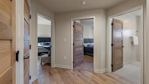 A hallway with wooden flooring leading to a bedroom with a bed and a nightstand. - Whispering Pines| Includes Two 1-Day Lift Tickets (Tamarack)