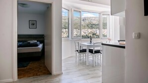 Une chambre moderne avec un lit, un coin repas avec des chaises et une vue sur la ville grâce à de grandes fenêtres.