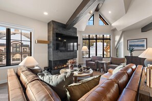 A modern living room with a fireplace, leather sofas, and large windows offering a view of a snowy landscape. - Granite Peak | Includes Two 1-Day Lift Tickets (Tamarack)