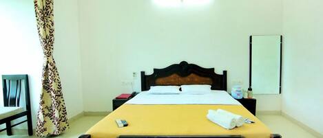 Habitación de hotel con cama, mesita de noche, lámpara, espejo, cortina y una silla.