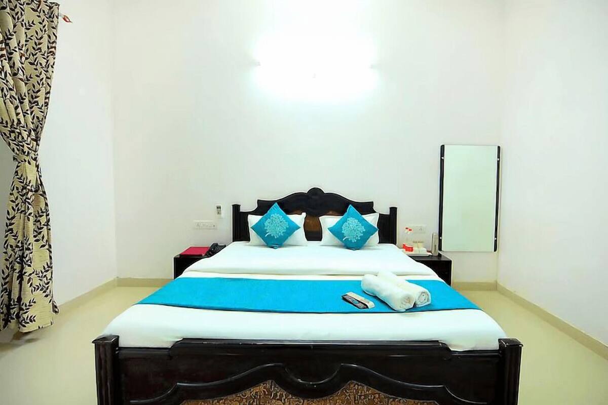 A neatly made bed with a blue bedspread and two decorative pillows, a bedside table with a lamp, and a wall-mounted mirror.