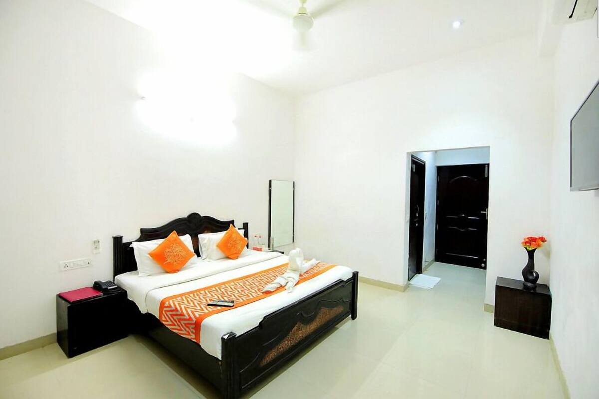 A hotel room with a bed, a bedside table, a nightstand, and a door leading to another room.