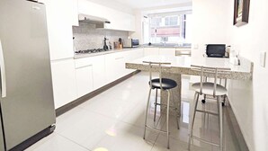 Une cuisine moderne avec des meubles blancs, un réfrigérateur en acier inoxydable, une cuisinière à gaz et un coin bar avec des tabourets.