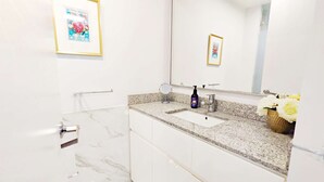 Une salle de bain moderne avec un sol en marbre, un comptoir en granit, un lavabo avec un robinet, un miroir et un tableau encadré au mur.