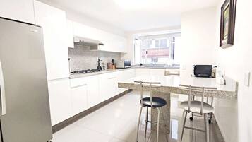 A modern kitchen with white cabinets, a stainless steel refrigerator, a granite countertop, and two bar stools.