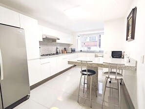 Eine moderne Küche mit weißen Schränken, einem Edelstahlkühlschrank, einer Granitabdeckung und zwei Barhocker.