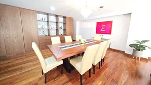 Un coin repas avec une table en bois, des chaises blanches, un lustre, une enseigne rouge et une plante en pot.